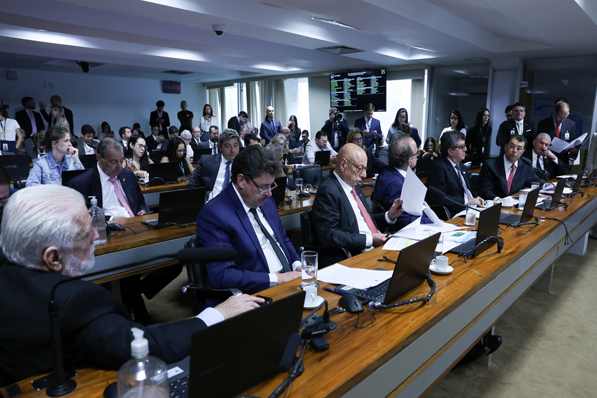 Parlamentares reunidos em comissão do Congresso analisando documentos e discutindo projeto de lei durante sessão legislativa.