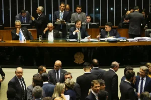 Parlamentares reunidos no plenário da Câmara dos Deputados durante sessão deliberativa, com mesa diretora e deputados em debate.