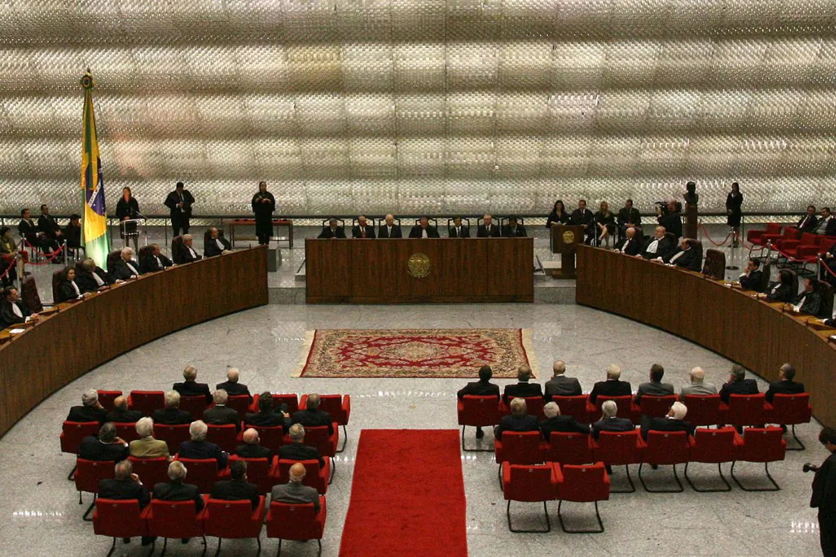 Sessão solene no plenário do Supremo Tribunal Federal, com ministros sentados em formato semicircular, cadeiras vermelhas e bandeira do Brasil ao fundo.