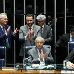Parlamentares aplaudem durante sessão no plenário do Congresso Nacional, com mesa diretora, documentos e computadores em uso.