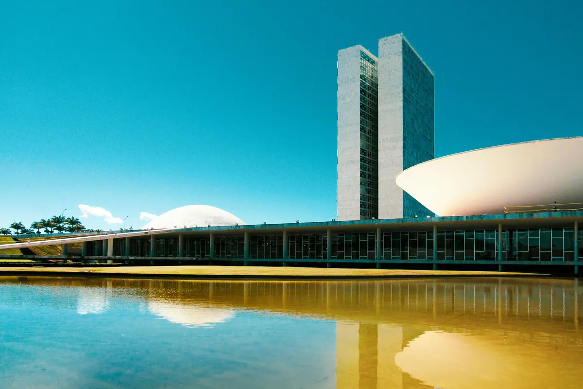 Congresso Nacional do Brasil em Brasília, com torres gêmeas, cúpulas da Câmara e do Senado refletidas no espelho d’água sob céu azul