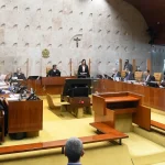 Plenário do Supremo Tribunal Federal com ministros togados durante sessão de julgamento, bandeira do Brasil e crucifixo ao fundo.