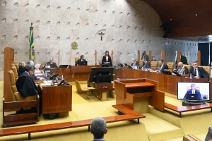 Plenário do Supremo Tribunal Federal com ministros togados durante sessão de julgamento, bandeira do Brasil e crucifixo ao fundo.