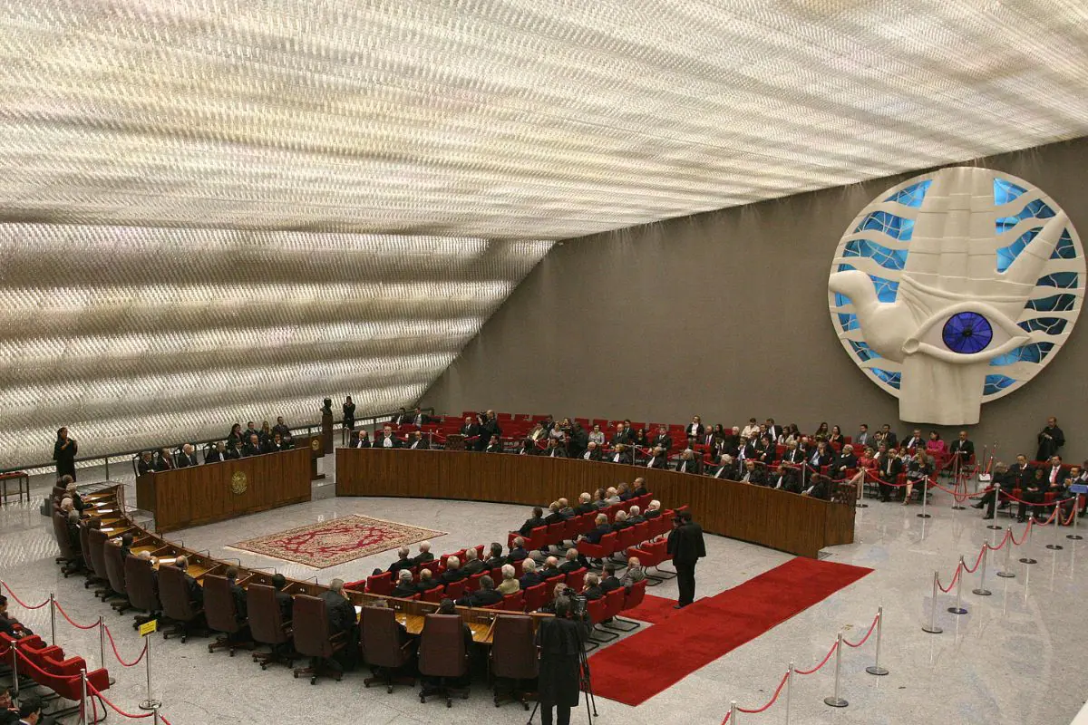 Plenário do Supremo Tribunal Federal em sessão de julgamento, com ministros sentados, cadeiras vermelhas, mesa em formato semicircular e escultura da Justiça ao fundo.