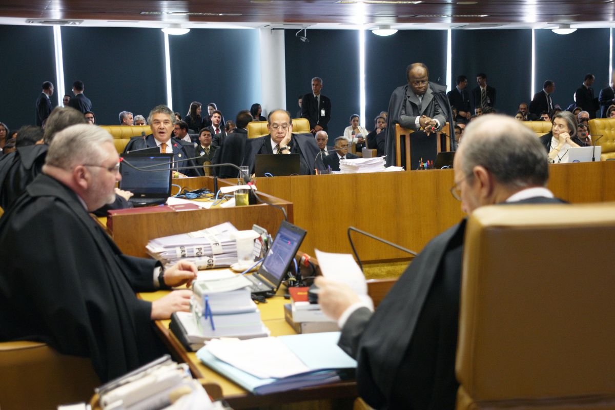 Sessão de julgamento no Tribunal Superior Eleitoral, com ministros togados, pilhas de processos, computadores e plenário cheio durante análise de caso eleitoral.
