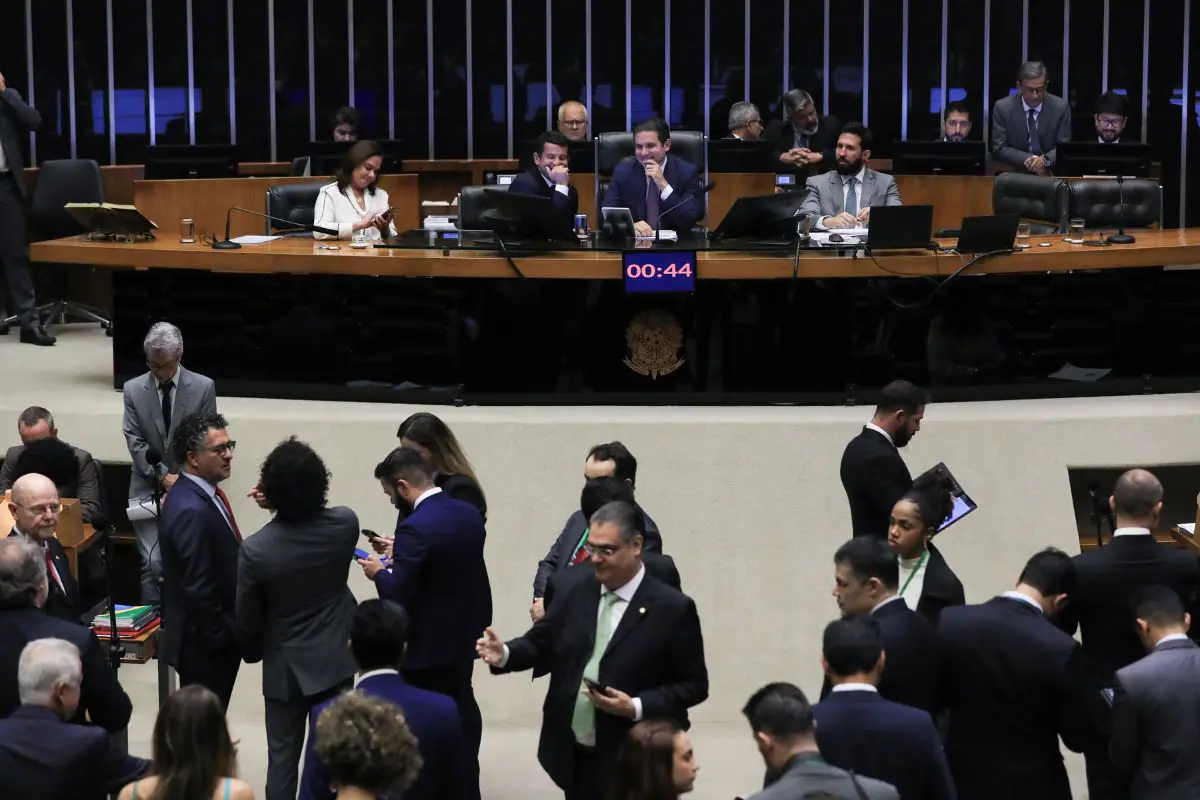 Plenário da Câmara dos Deputados durante sessão sobre impostos no Brasil, com parlamentares reunidos, mesa diretora ao fundo e painel de tempo em destaque.