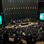 Plenário do Congresso Nacional lotado durante sessão solene, com autoridades reunidas à mesa diretora e bandeira do Brasil exibida em painéis.