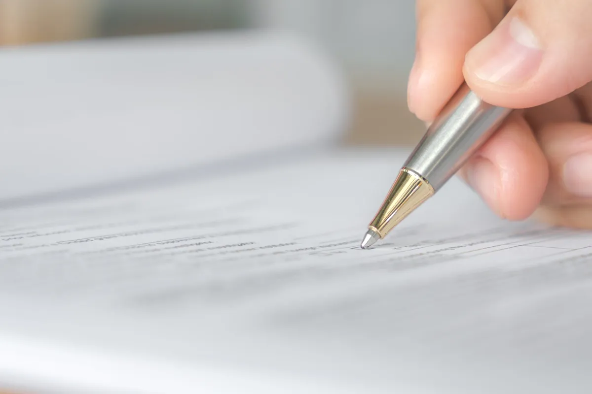 Mão segurando caneta assinando documento oficial em formulário impresso, representando ato administrativo ou jurídico.