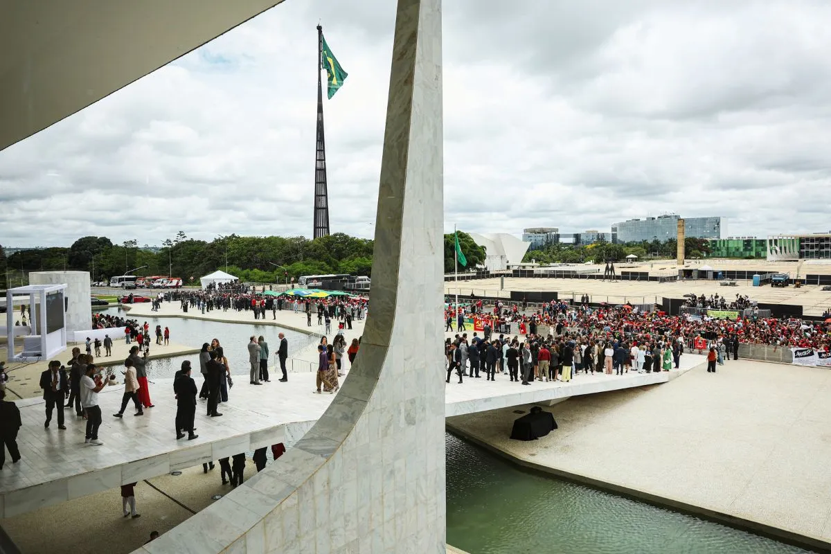 Multidão reunida na Praça dos Três Poderes, em Brasília, com bandeira do Brasil ao fundo durante ato público ao ar livre.