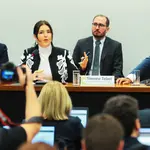 Autoridade feminina fala em audiência pública sobre orçamento público, sentada à mesa com parlamentares, microfones e público acompanhando.