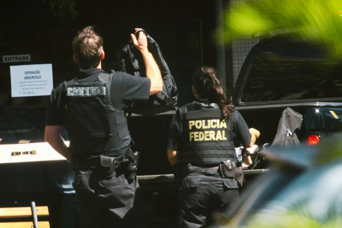 Agentes da Polícia Federal em operação oficial, usando coletes identificados, durante cumprimento de mandado em área urbana.
