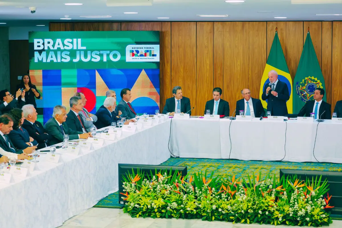 Reunião do governo federal com autoridades e ministros, bandeiras do Brasil ao fundo e painel “Brasil Mais Justo”