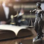 Estátua da deusa da justiça com balança e olhos vendados sobre um livro aberto, representando projeto de lei, processo legislativo e aplicação da lei.