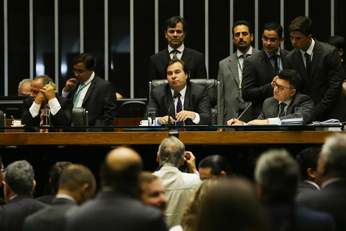 Sessão deliberativa com autoridades sentadas à mesa diretora enquanto público acompanha debate em plenário