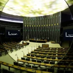 Plenário legislativo amplo com bancadas vazias e mesa diretora preparada para sessão oficial