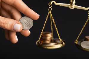 Pessoa equilibra moedas em uma balança, em representação ao déficit fiscal no Brasil