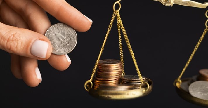 Pessoa equilibra moedas em uma balança, em representação ao déficit fiscal no Brasil