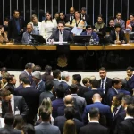Sessão de votação em plenário com autoridades na mesa diretora e grande concentração de parlamentares no ambiente