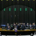 Mesa diretora em plenário legislativo com parlamentares reunidos durante momento decisivo da sessão