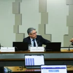 Senadores participam de audiência pública em comissão parlamentar, com notebooks e microfones durante debate oficial