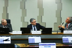 Senadores participam de audiência pública em comissão parlamentar, com notebooks e microfones durante debate oficial