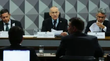 Presidente de comissão parlamentar fala ao microfone durante audiência pública no Senado, com documentos sobre a mesa