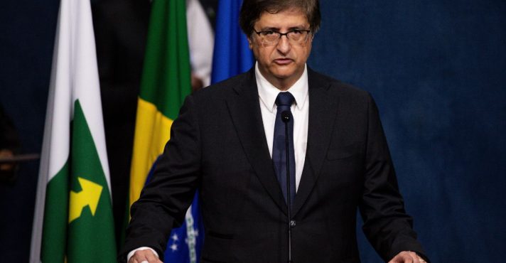 Autoridade brasileira discursando em tribuna durante pronunciamento oficial, com bandeiras ao fundo.