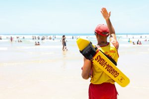 Bombeiro acena para banhista em praia do litoral de São Paulo | Foto: Divulgação/Agência SP