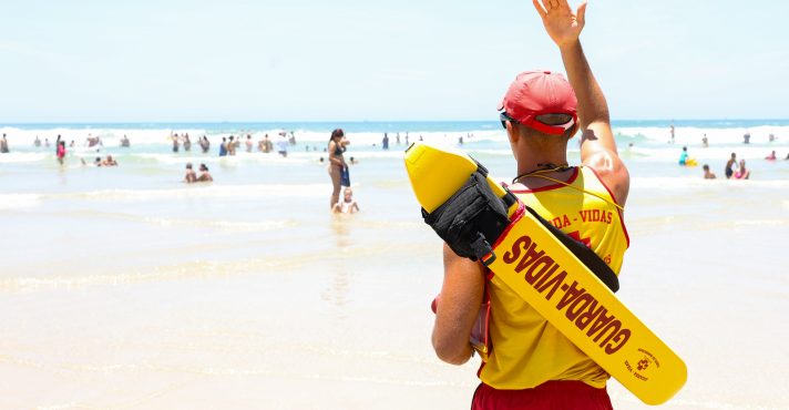 Bombeiro acena para banhista em praia do litoral de São Paulo | Foto: Divulgação/Agência SP