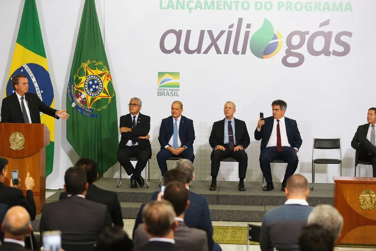 Autoridades em cerimônia oficial de lançamento do programa Auxílio Gás com bandeiras do Brasil ao fundo