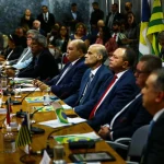 Autoridades brasileiras participam de reunião oficial com bandeiras estaduais e do Brasil ao fundo.