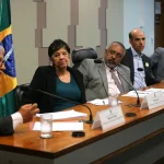 Autoridades participam de audiência no Congresso Nacional para discutir crise política, com mesa diretora e bandeira do Brasil ao fundo.