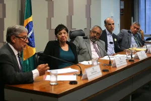 Autoridades participam de audiência no Congresso Nacional para discutir crise política, com mesa diretora e bandeira do Brasil ao fundo.