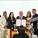 Grupo de autoridades reunidas durante cerimônia oficial, exibindo documento assinado em ato institucional