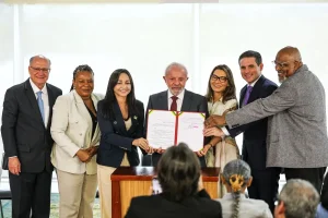 Grupo de autoridades reunidas durante cerimônia oficial, exibindo documento assinado em ato institucional