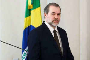 Autoridade brasileira de terno em pronunciamento oficial com bandeira do Brasil ao fundo.