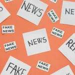 Papéis com as palavras fake news, news e real espalhados sobre fundo laranja representando desinformação