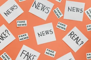 Papéis com as palavras fake news, news e real espalhados sobre fundo laranja representando desinformação