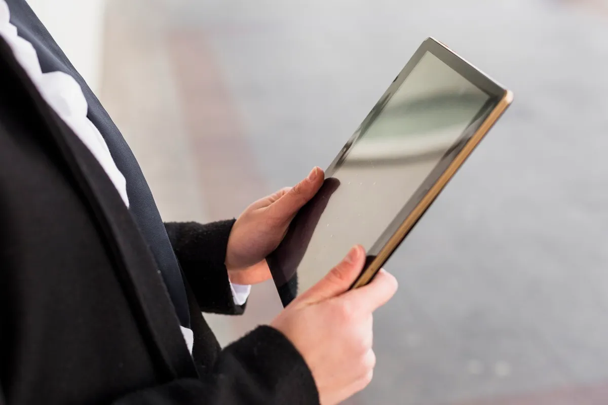 Pessoa segurando tablet e acessando conteúdo digital em ambiente externo
