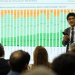 Palestrante apresentando gráfico sobre matrículas na educação básica no Brasil para público em auditório.