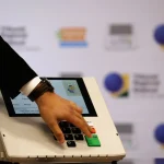 Mão de eleitor digitando números em urna eletrônica durante processo eleitoral