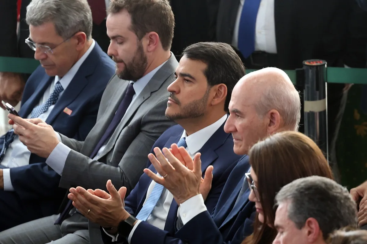 Autoridades políticas sentadas em cerimônia oficial aplaudem durante evento institucional do governo.