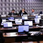 Autoridades reunidas em sessão institucional durante inquérito com uso de computadores e documentos