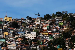 Helicóptero sobrevoa comunidade em área de favela no Brasil com casas densamente construídas em morro.