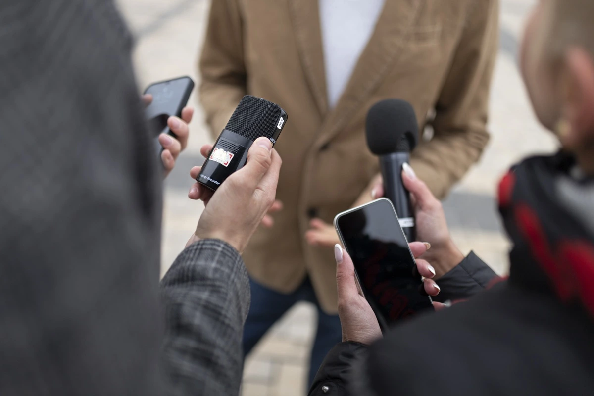 Jornalistas seguram microfones e celulares durante entrevista em cobertura de notícia política ao ar livre.