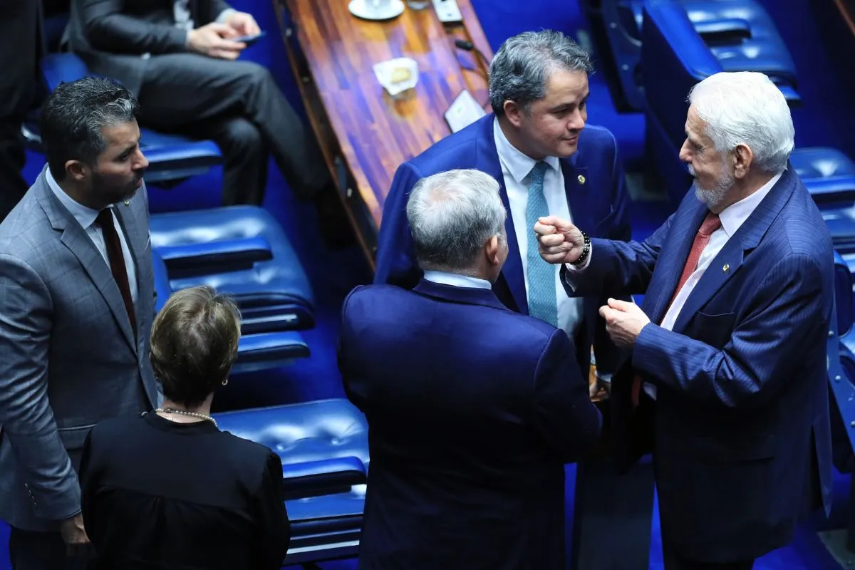 Parlamentares conversam em pé no plenário do Senado Federal durante sessão legislativa, em momento de articulação política.