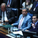 Senadores participam de sessão no plenário do Senado Federal, com parlamentares sentados à mesa e um deles discursando.