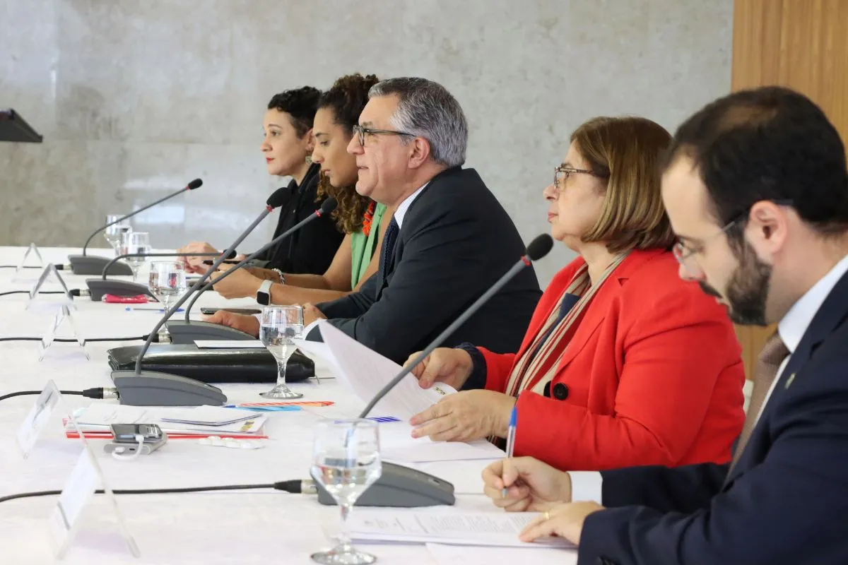 Autoridades sentadas em mesa com microfones durante audiência pública para discussão de políticas públicas no Brasil.