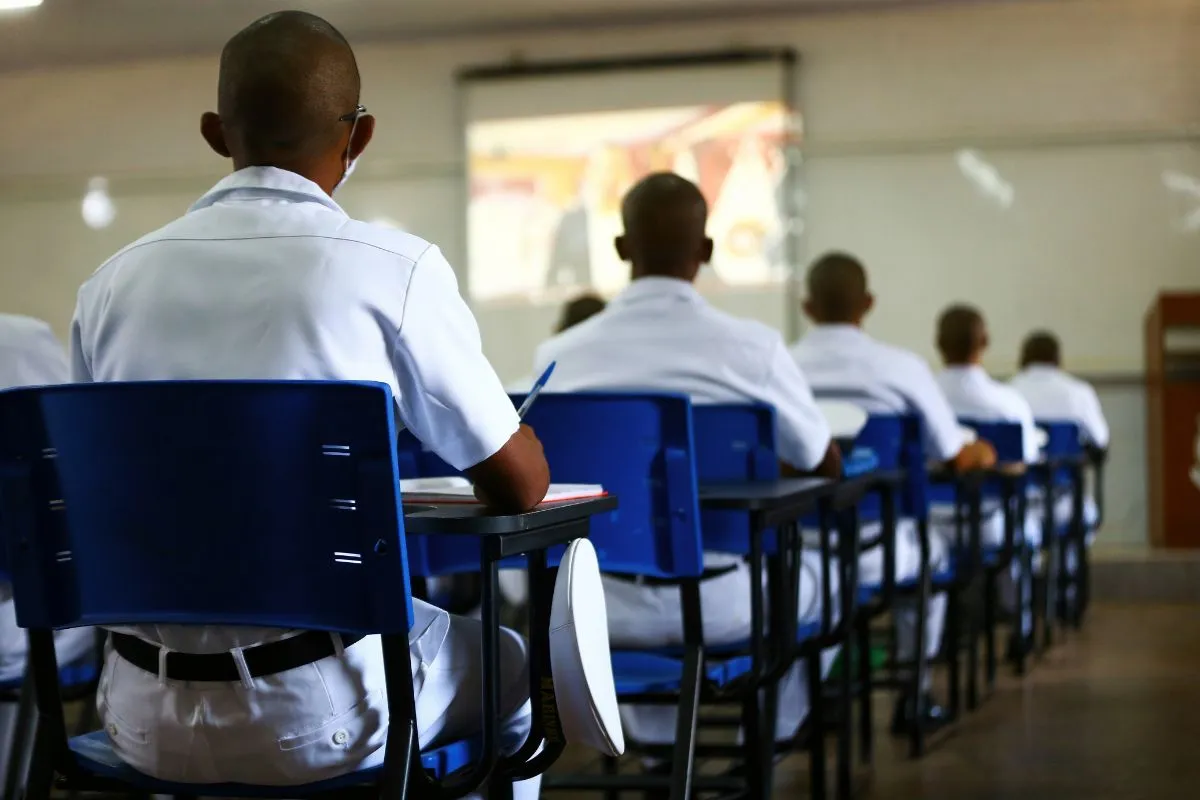 Estudantes uniformizados sentados em sala de aula assistindo aula com projeção na lousa