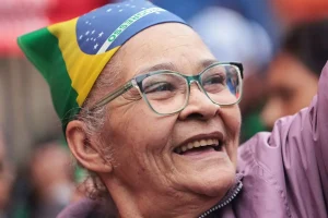 Senhora idosa sorrindo com óculos e usando bandana com a bandeira do Brasil durante manifestação patriótica